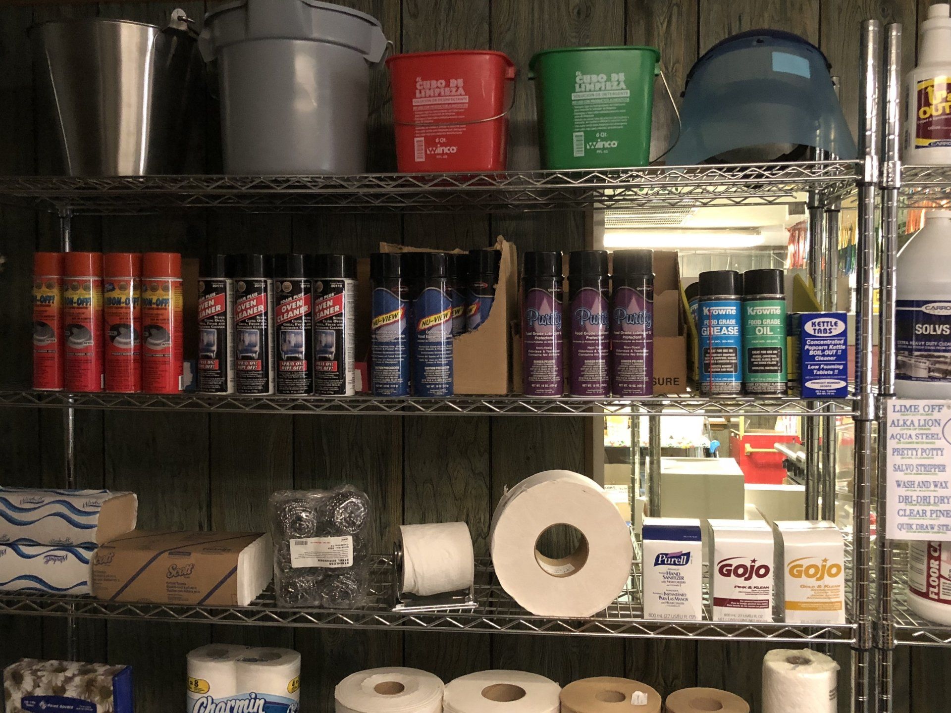 A shelf full of cleaning supplies including spray bottles and toilet paper