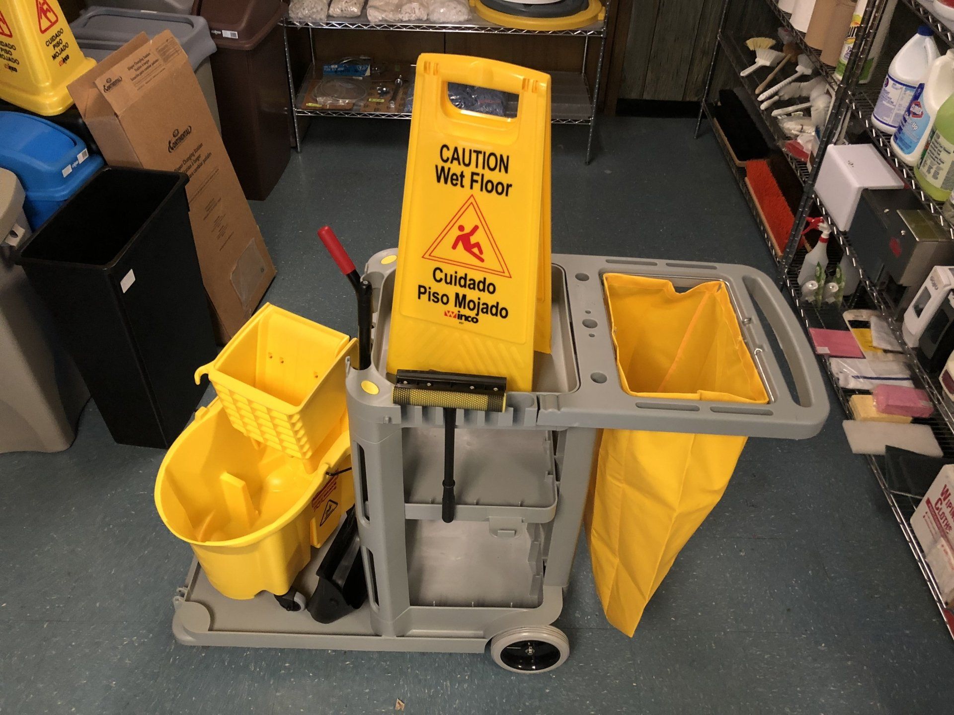 A cleaning cart with a yellow sign that says caution wet floor