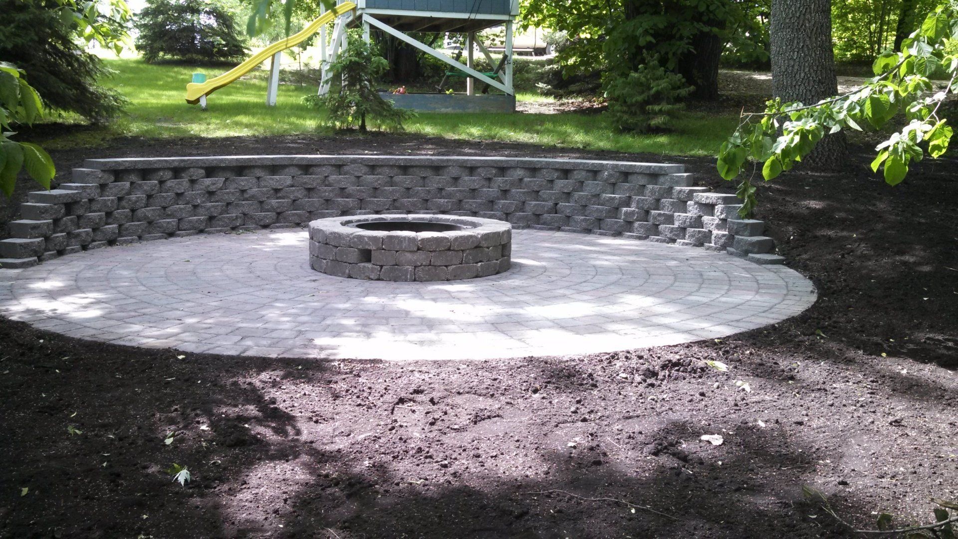 A fire pit is surrounded by a stone wall in a backyard.