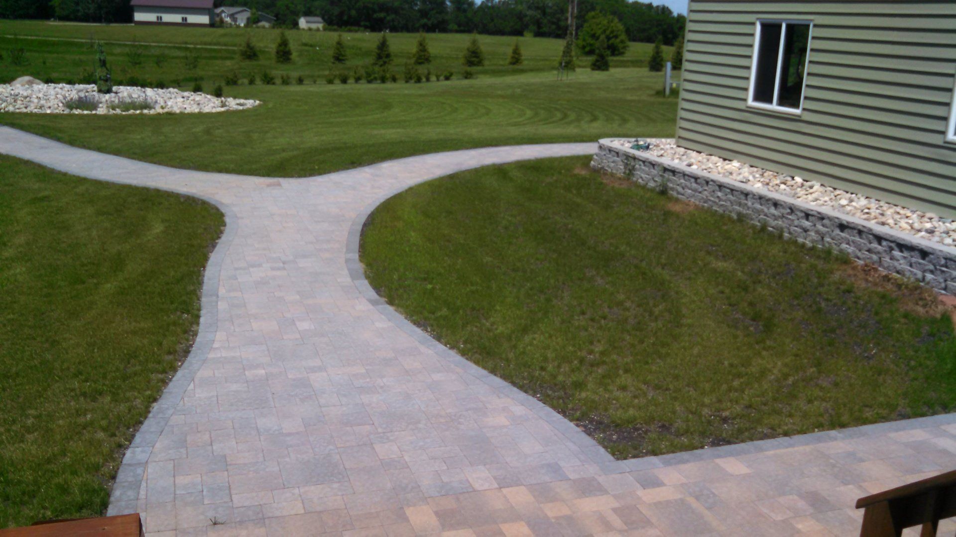 A brick walkway going through a grassy field next to a house.