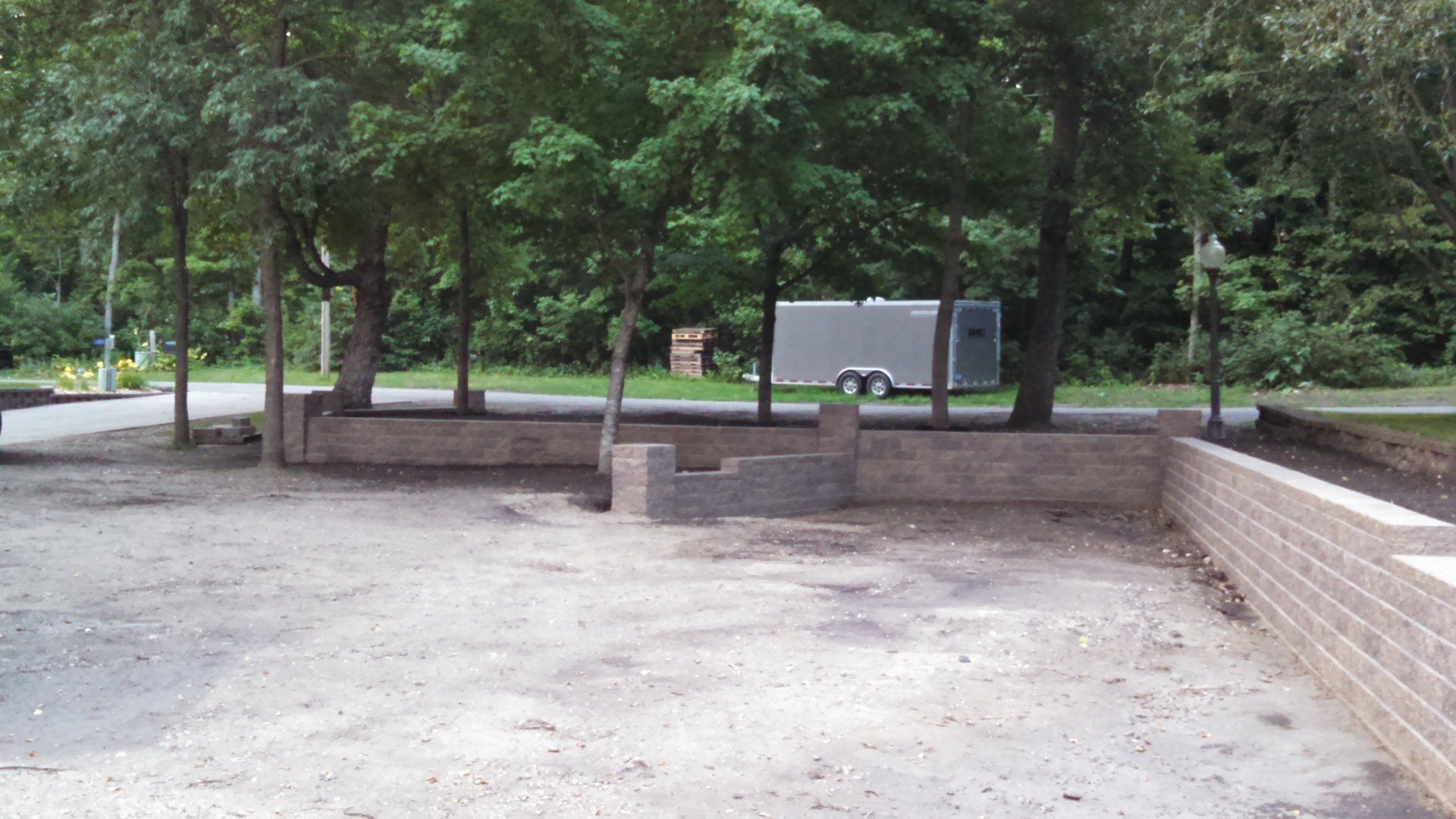 An empty parking lot with trees and a trailer in the background.