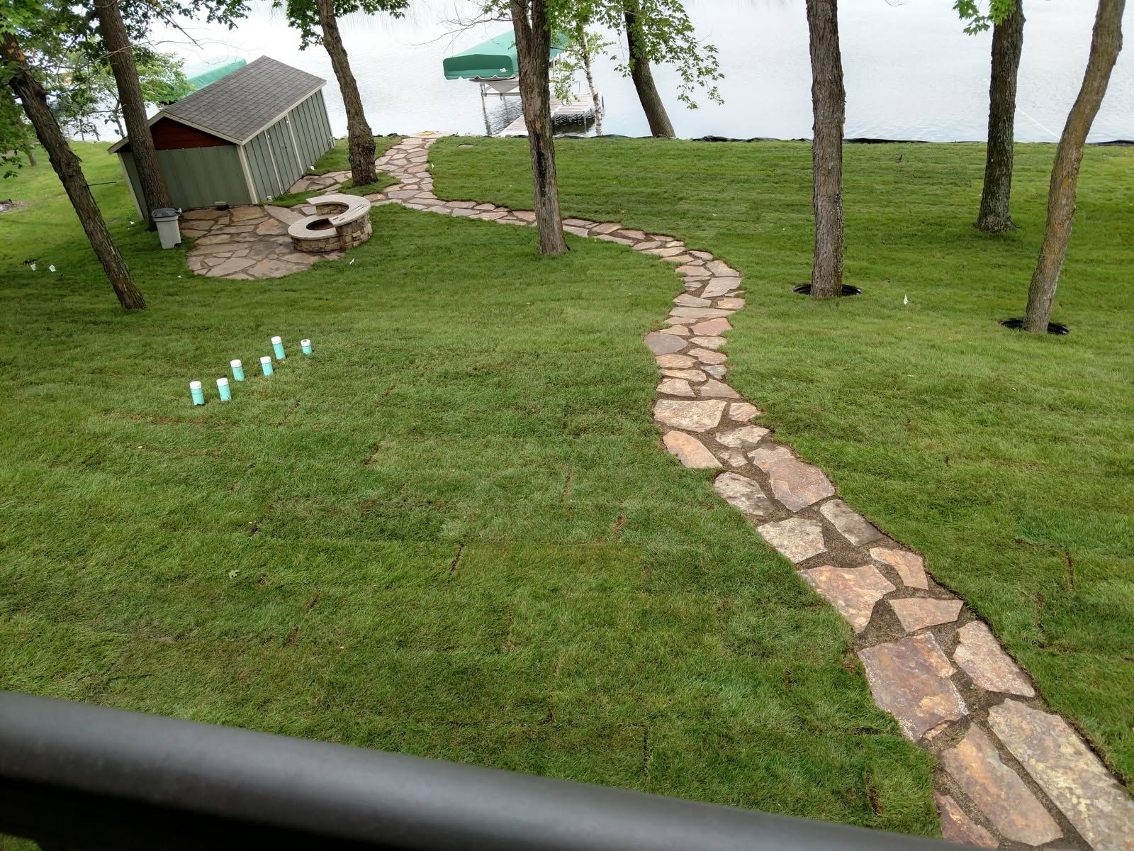 A stone walkway leading to a lake with a shed in the background.