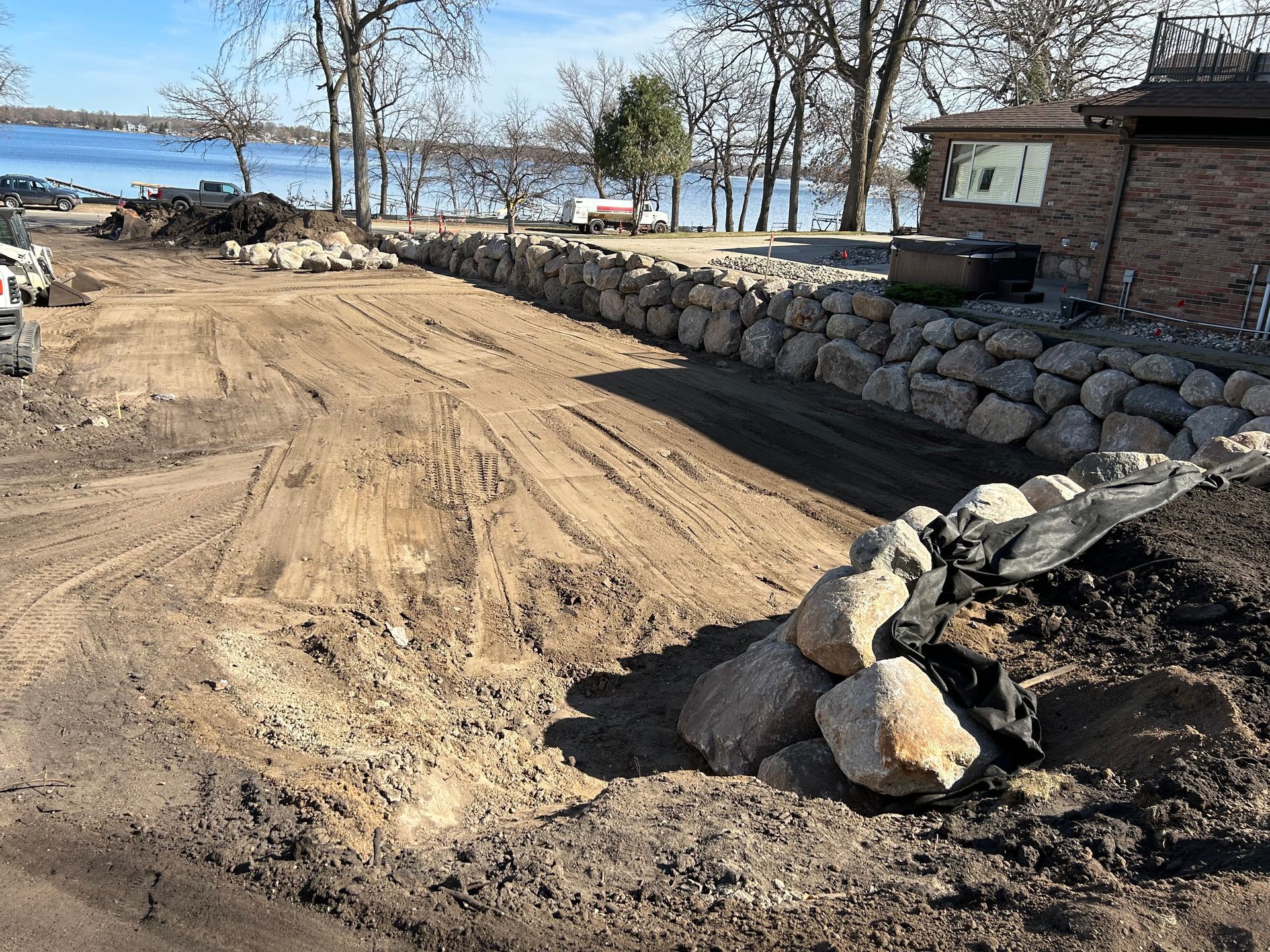 A dirt road with a stone wall along the side of it next to a body of water.