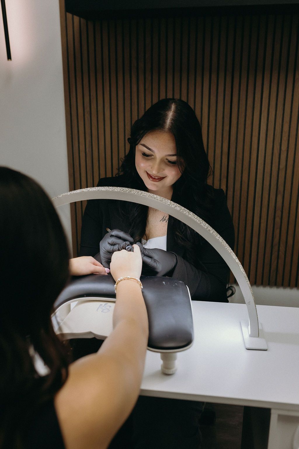 A woman wearing a black tank top and a necklace is smiling in front of a holographic background.