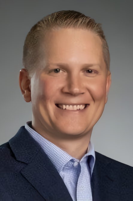 A man in a suit and blue shirt is smiling for the camera.