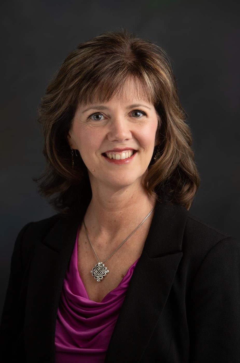 A woman wearing a black jacket and a purple shirt is smiling for the camera.