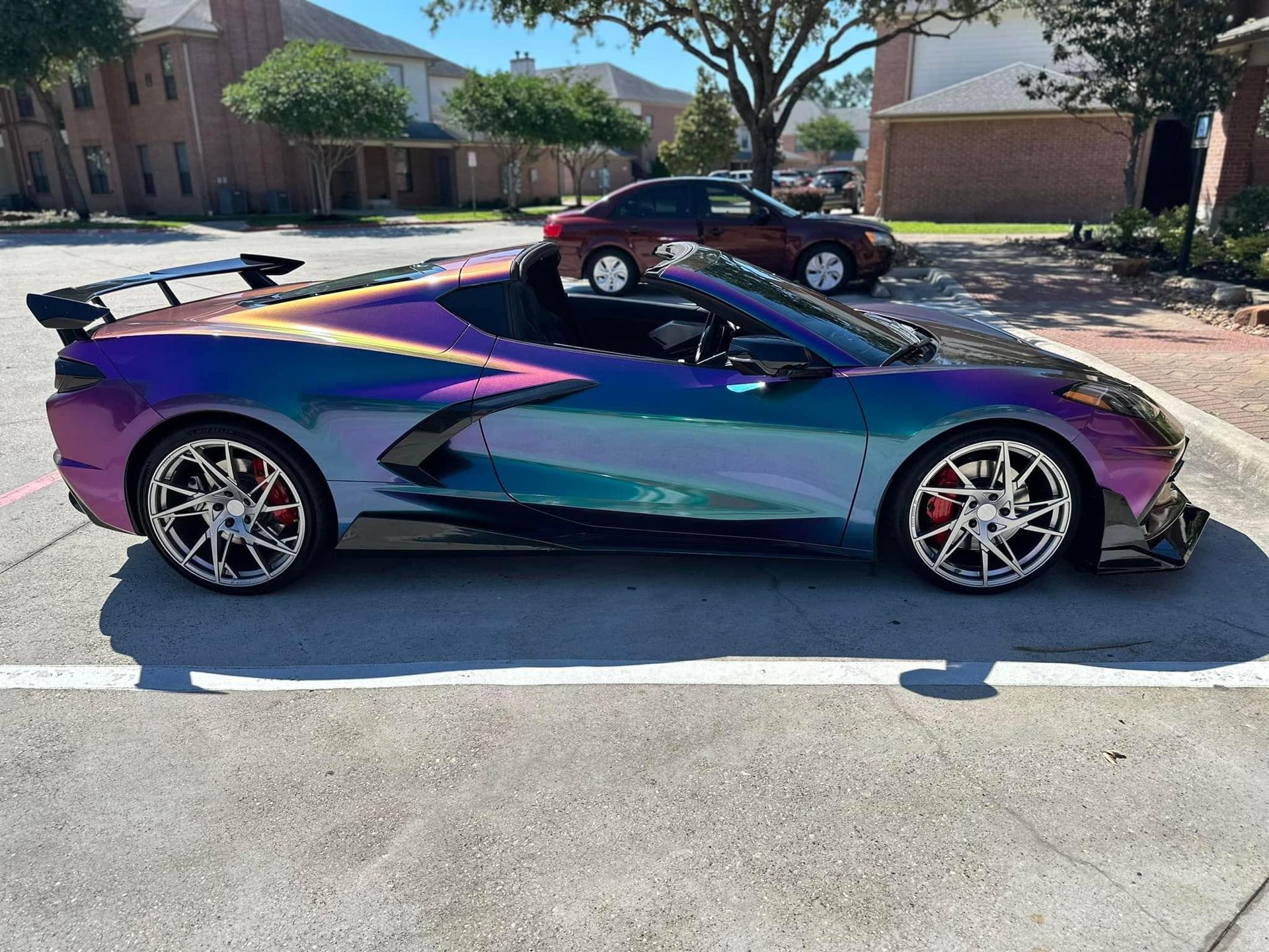 A custom iridescent Chevrolet Corvette convertible parked on an asphalt lot.