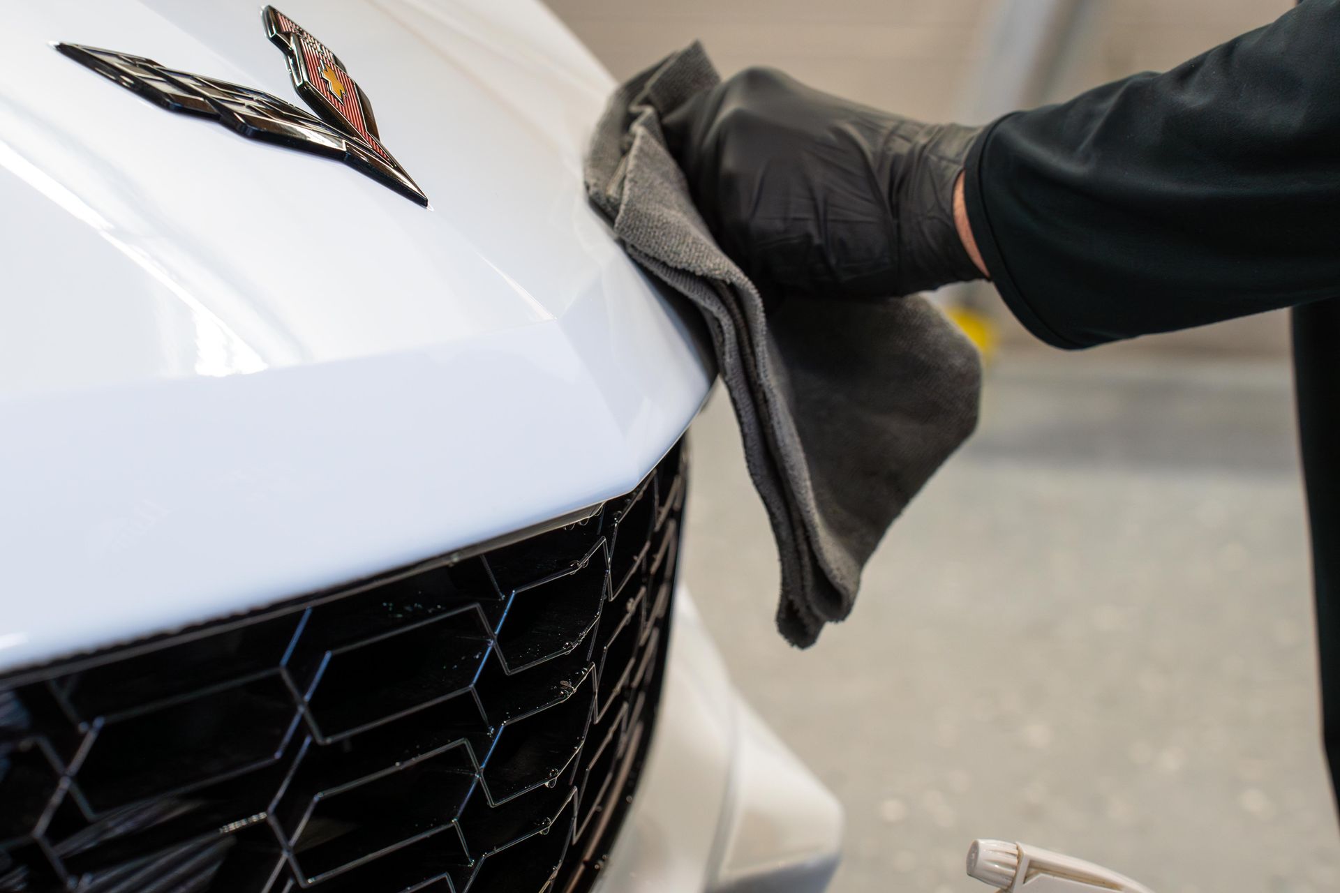 Gloved hand wiping a white car hood with a microfiber cloth; black grille and emblem visible.