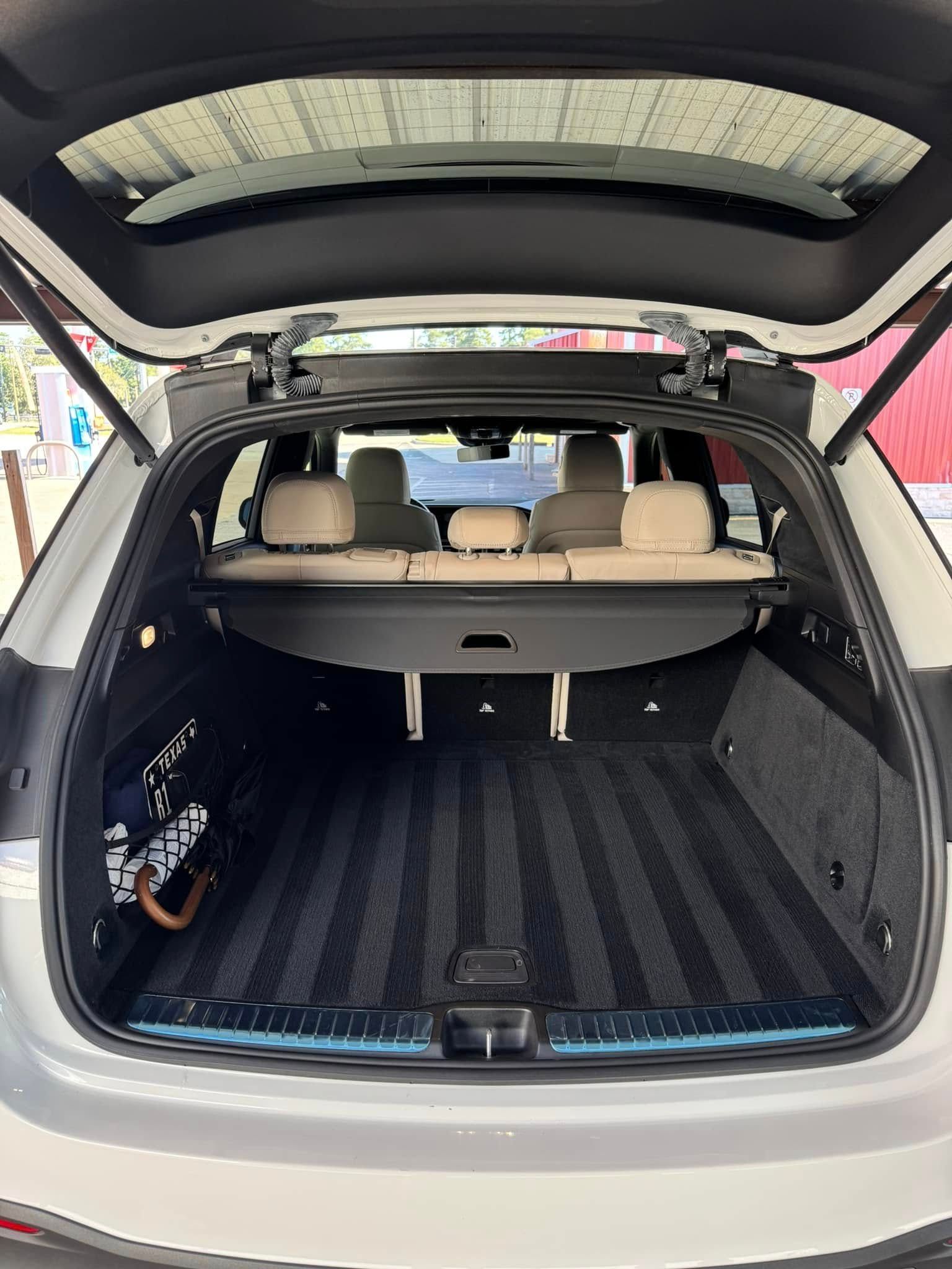 Open rear cargo area of a white SUV with beige interior, showing seats and cargo space with a rolled-up cover.