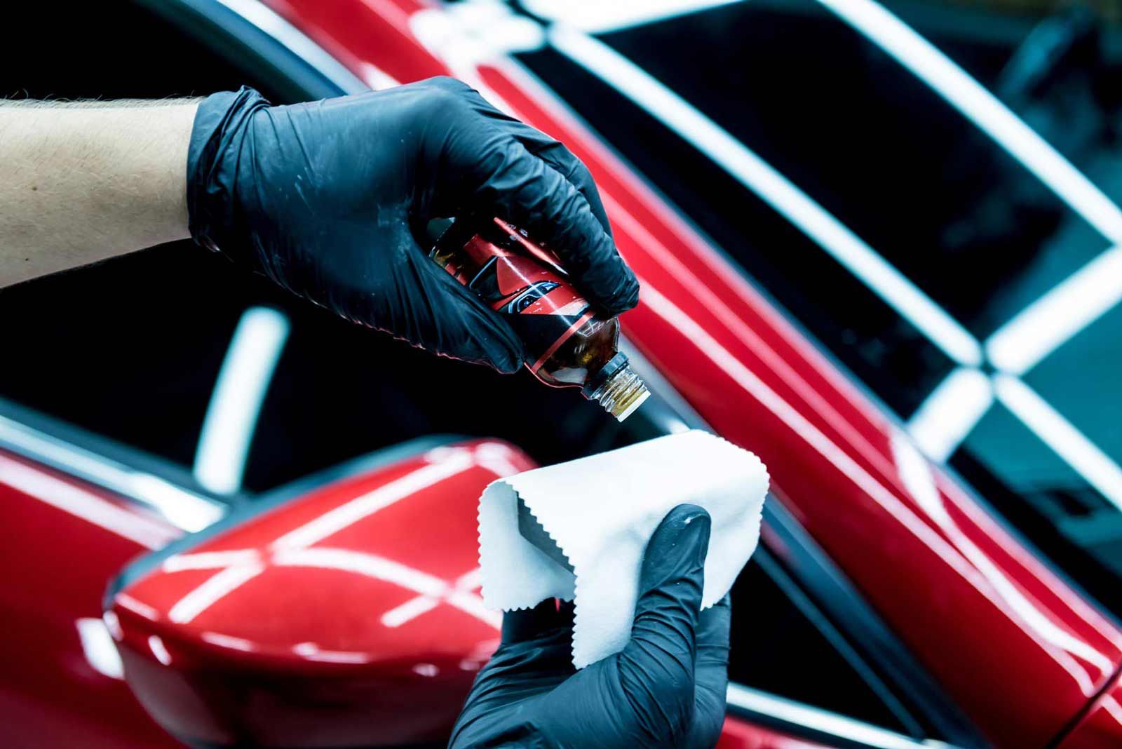Person in black gloves applying coating to car with a microfiber cloth.