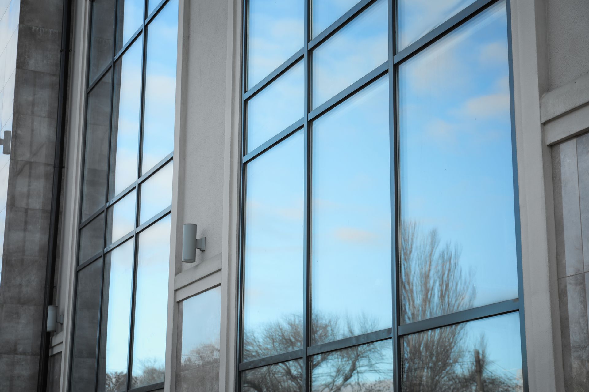 Large glass windows reflecting a blue sky and bare trees, set in a building facade.