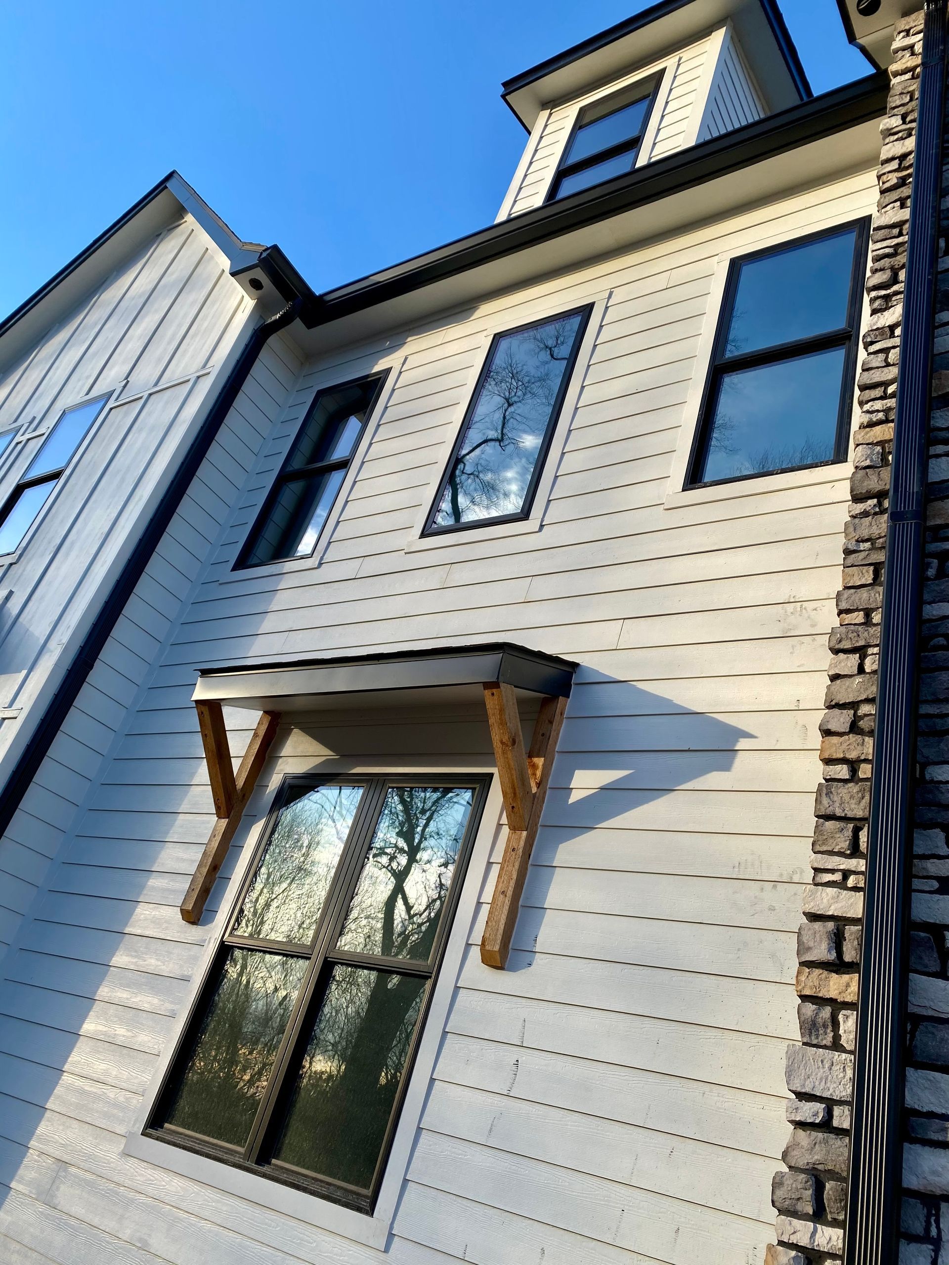 White house with black-framed windows, wood awning, and stone chimney against a blue sky.