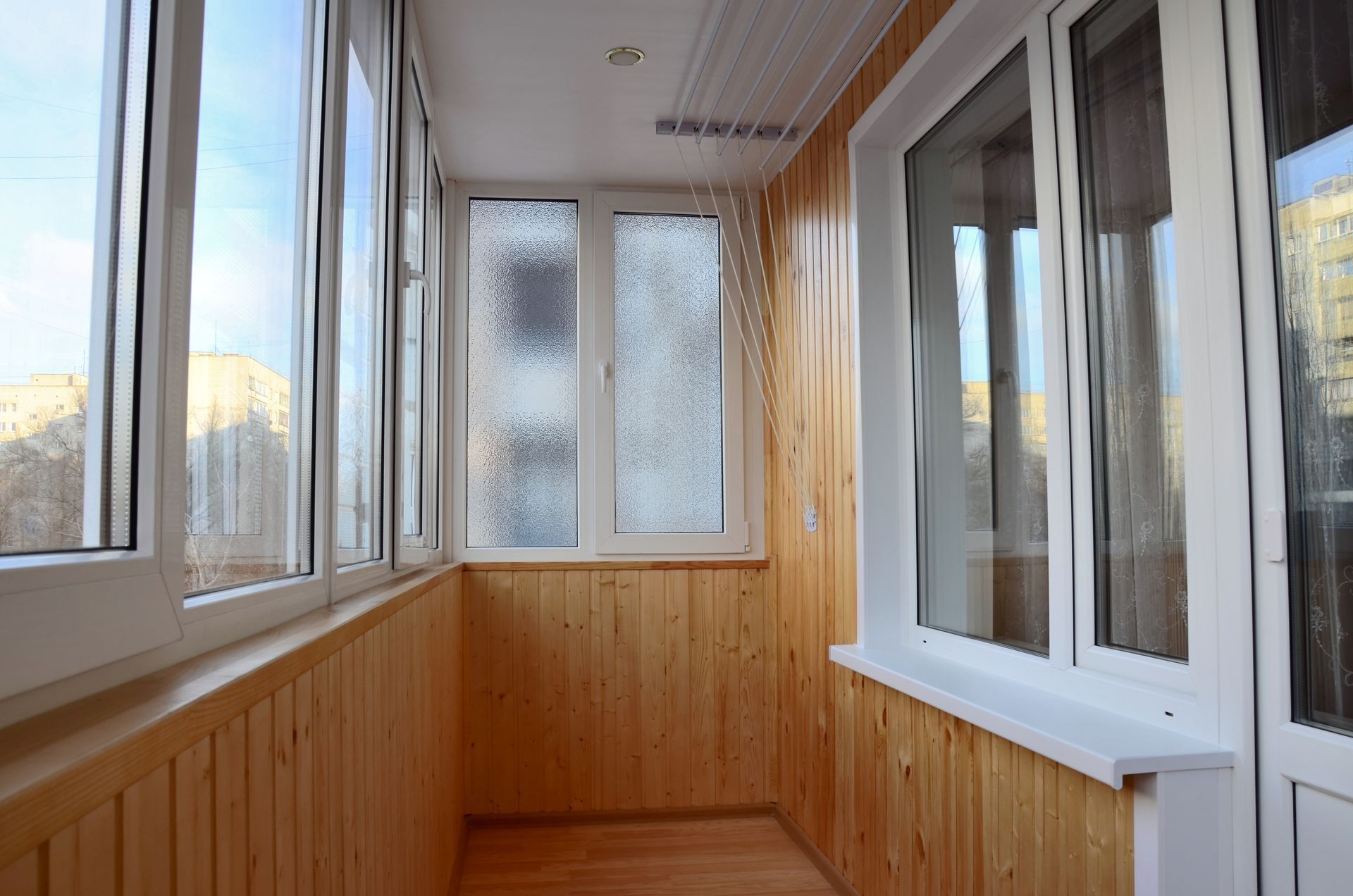 Interior of a sunroom/balcony with wood paneling, multiple windows, and a white ceiling.
