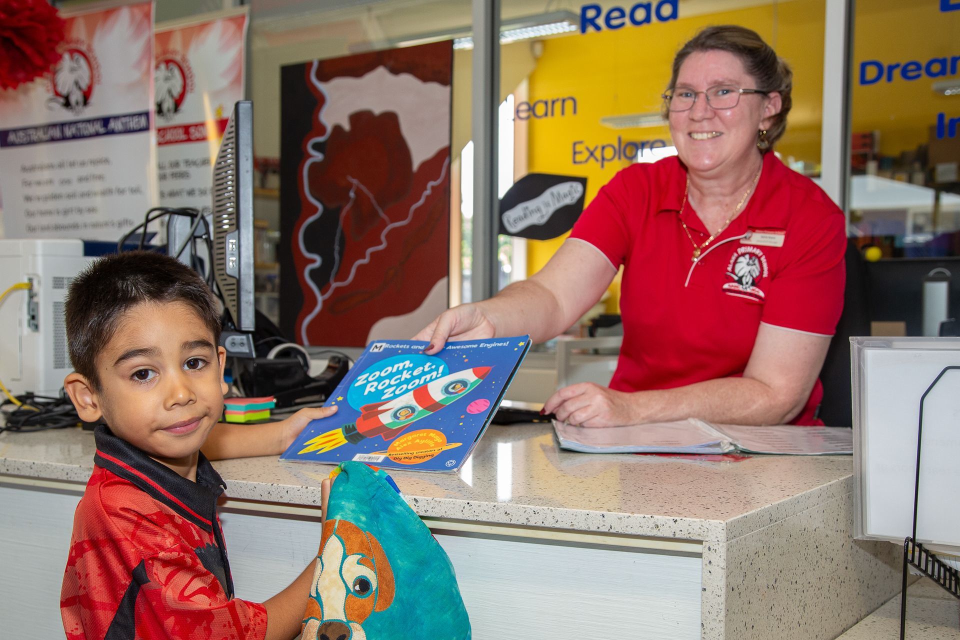 A child receiving a book from a library worker behind a counter.