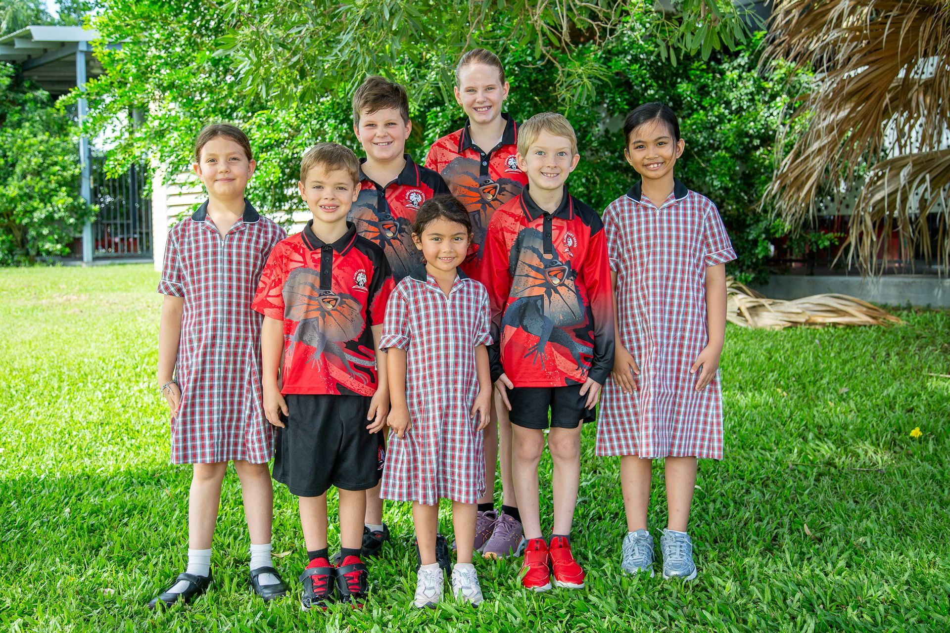 Group of children in school uniforms and sports shirts, standing on grass.