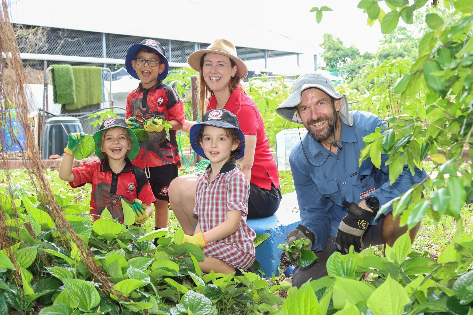 Boy in hat tending to a plant in a garden, near a green tub.