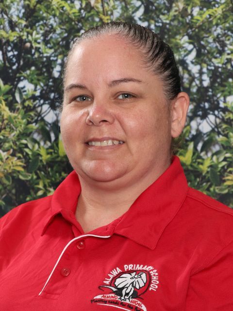 Woman in a red polo shirt smiling, with the logo of Akora Primary School.