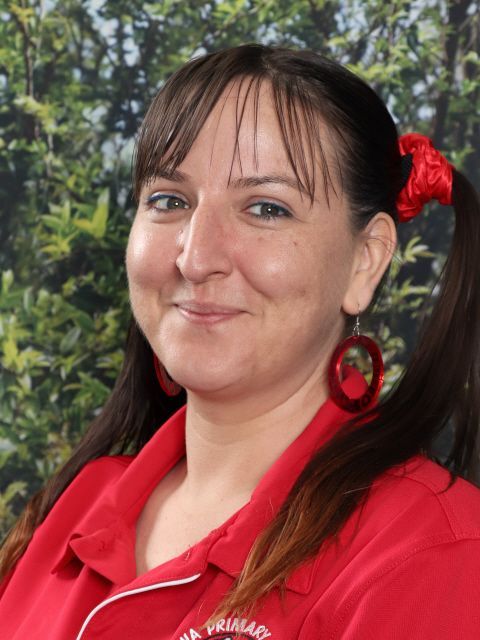 Woman with dark hair in pigtails, wearing a red shirt and hoop earrings, smiling.