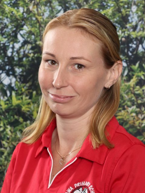 Woman in a red polo shirt with a logo smiles in front of a green foliage background.