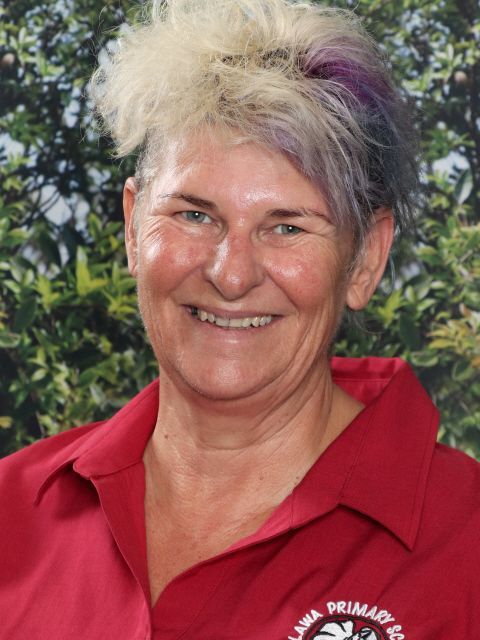 Woman with spiky, multi-colored hair smiles, wearing a red polo shirt; backdrop of green plants.