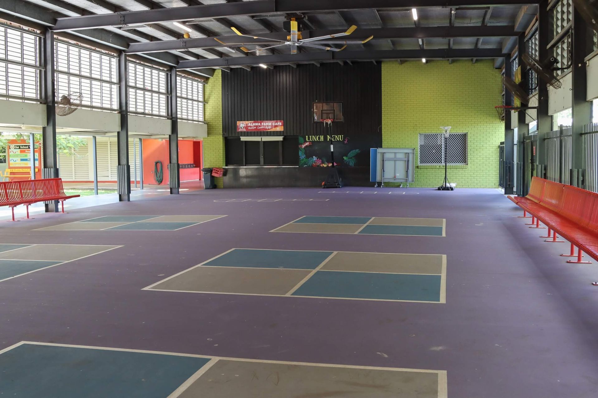 Indoor rec space with purple floor, painted squares, basketball hoop, and red benches.