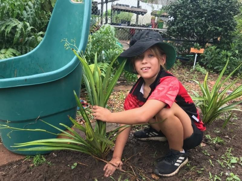 Boy in hat tending to a plant in a garden, near a green tub.