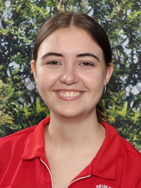 Smiling young woman with brown hair in a red collared shirt, outdoors.