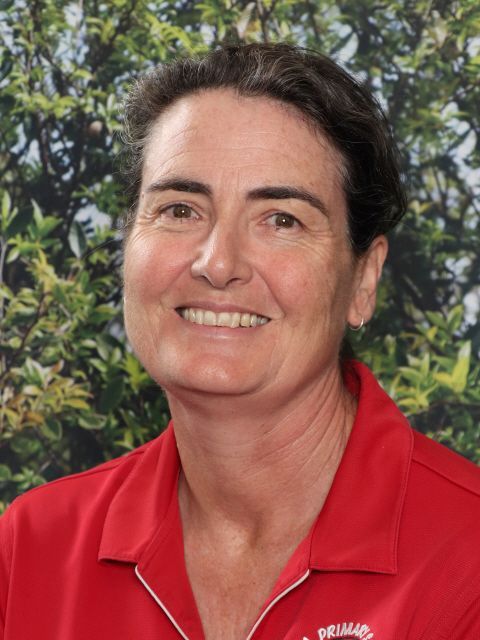 Woman with dark hair, smiling, wearing a red polo shirt in front of a green background.