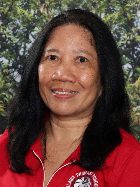 Woman with long dark hair, wearing a red shirt, smiles at the camera, in front of a green and brown backdrop.
