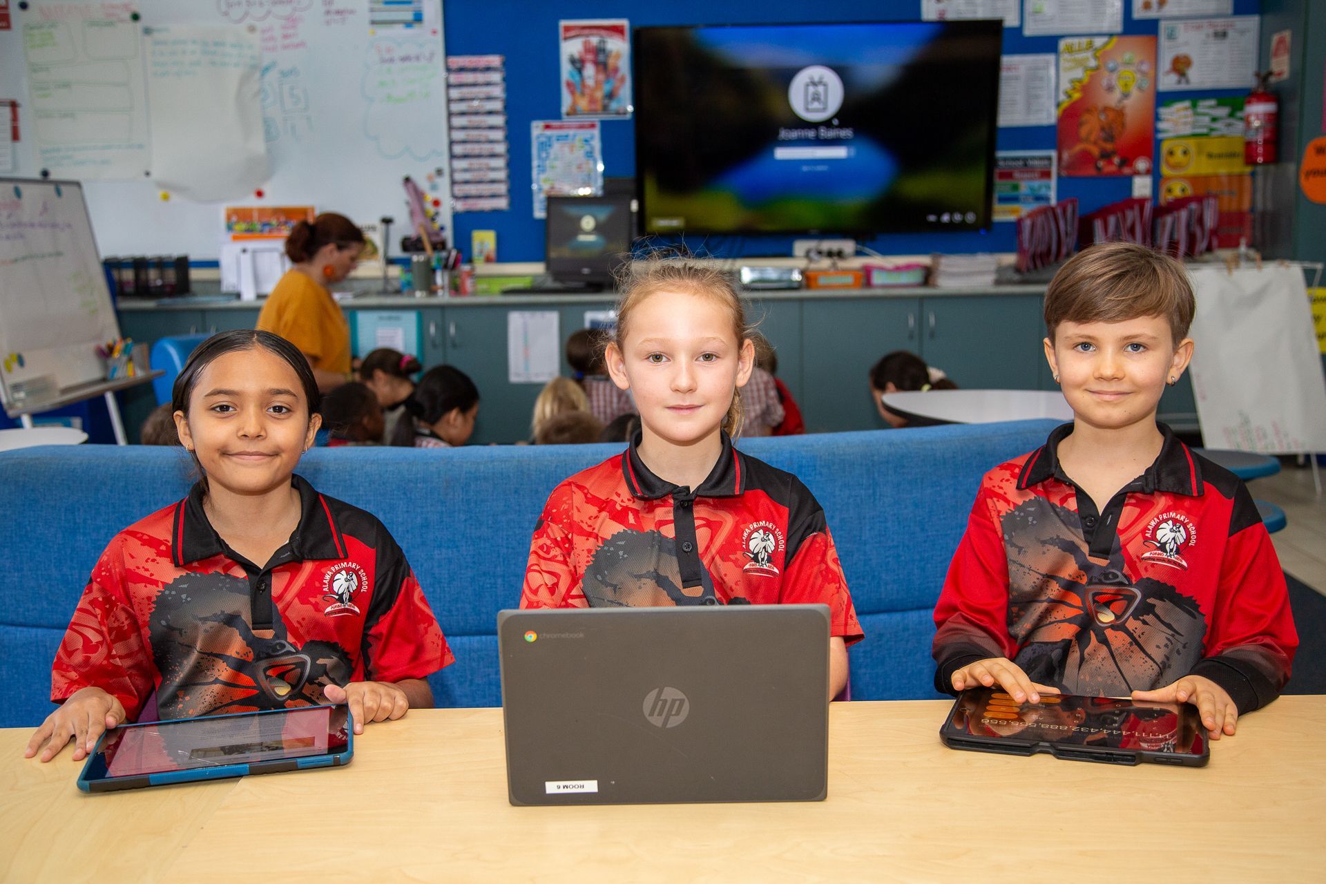 Three students with tech devices in a classroom, looking at the camera.