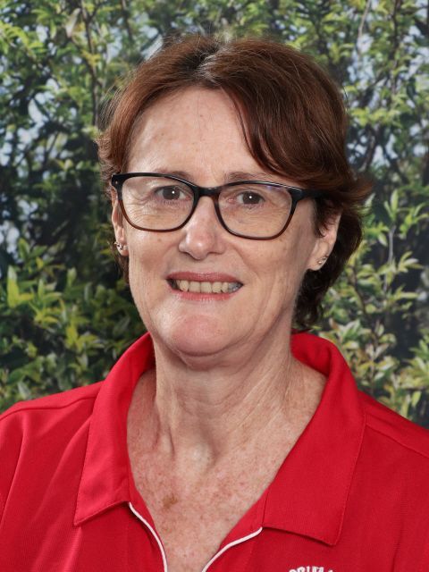 Woman with glasses and short red hair, wearing a red polo shirt, smiling, against a green background.