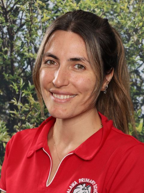 Woman in red shirt with logo smiles, outdoors.