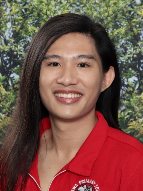 Person with long dark hair, smiling, wearing a red polo shirt, against a blurred leafy background.