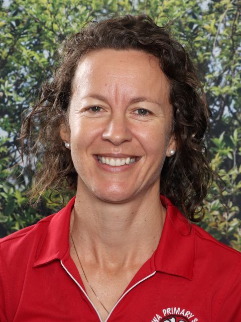 Woman in a red polo shirt smiling, with the logo of Akora Primary School.