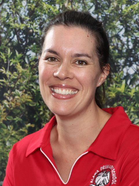 Woman smiling in red polo shirt, set against greenery.