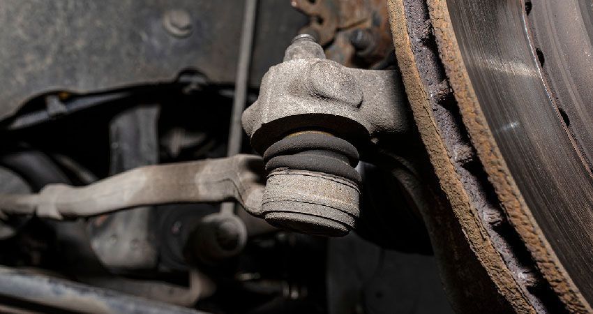 Close-up of a worn tie rod end, connected to a brake rotor, in an automotive setting.