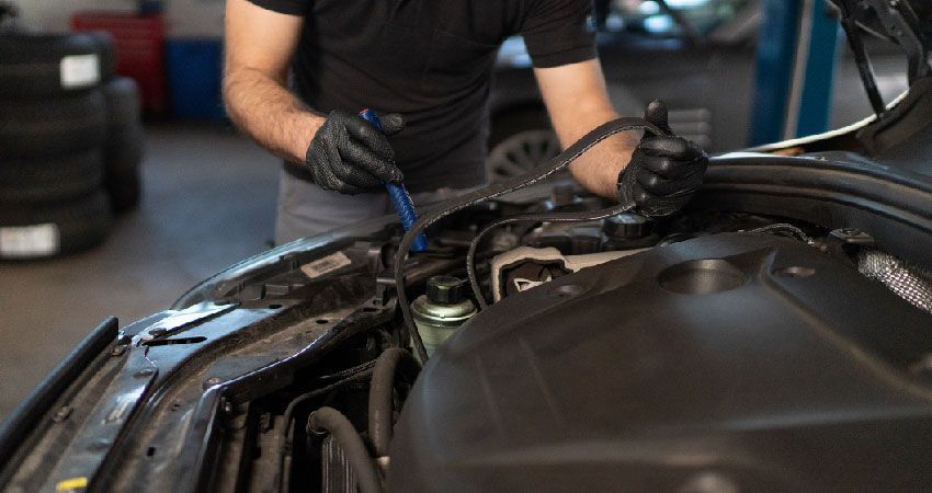 Mechanic inspecting car engine with a tool, wearing gloves, in a garage.