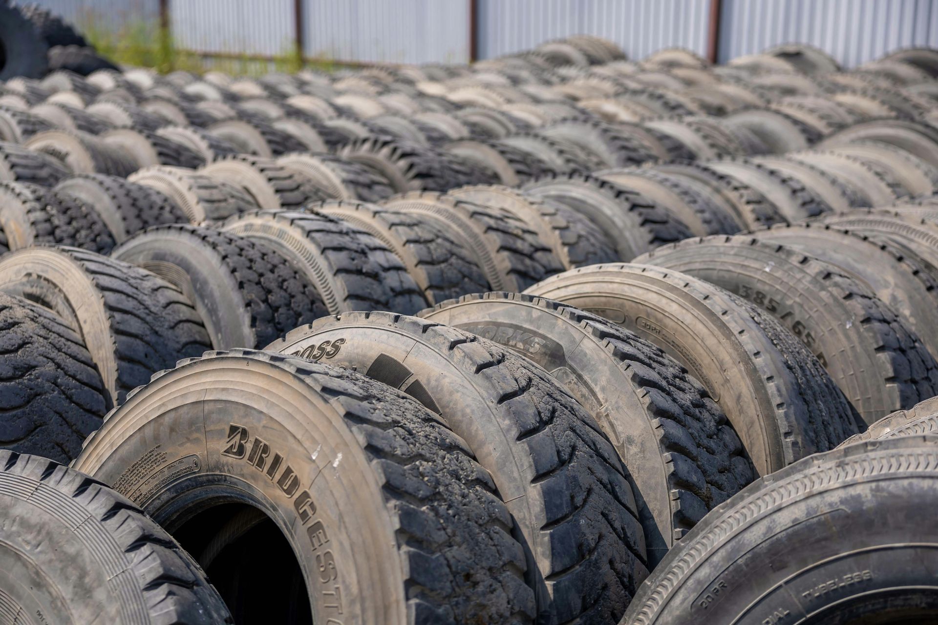 Rows of used tires stacked outdoors, likely at a tire disposal or recycling facility.