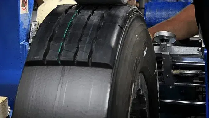 A large black tire is being inspected by a machine, likely for quality control.