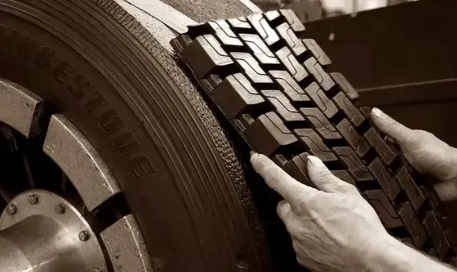 Hands holding a section of a black tire tread, placing it on a tire rim, sepia toned.