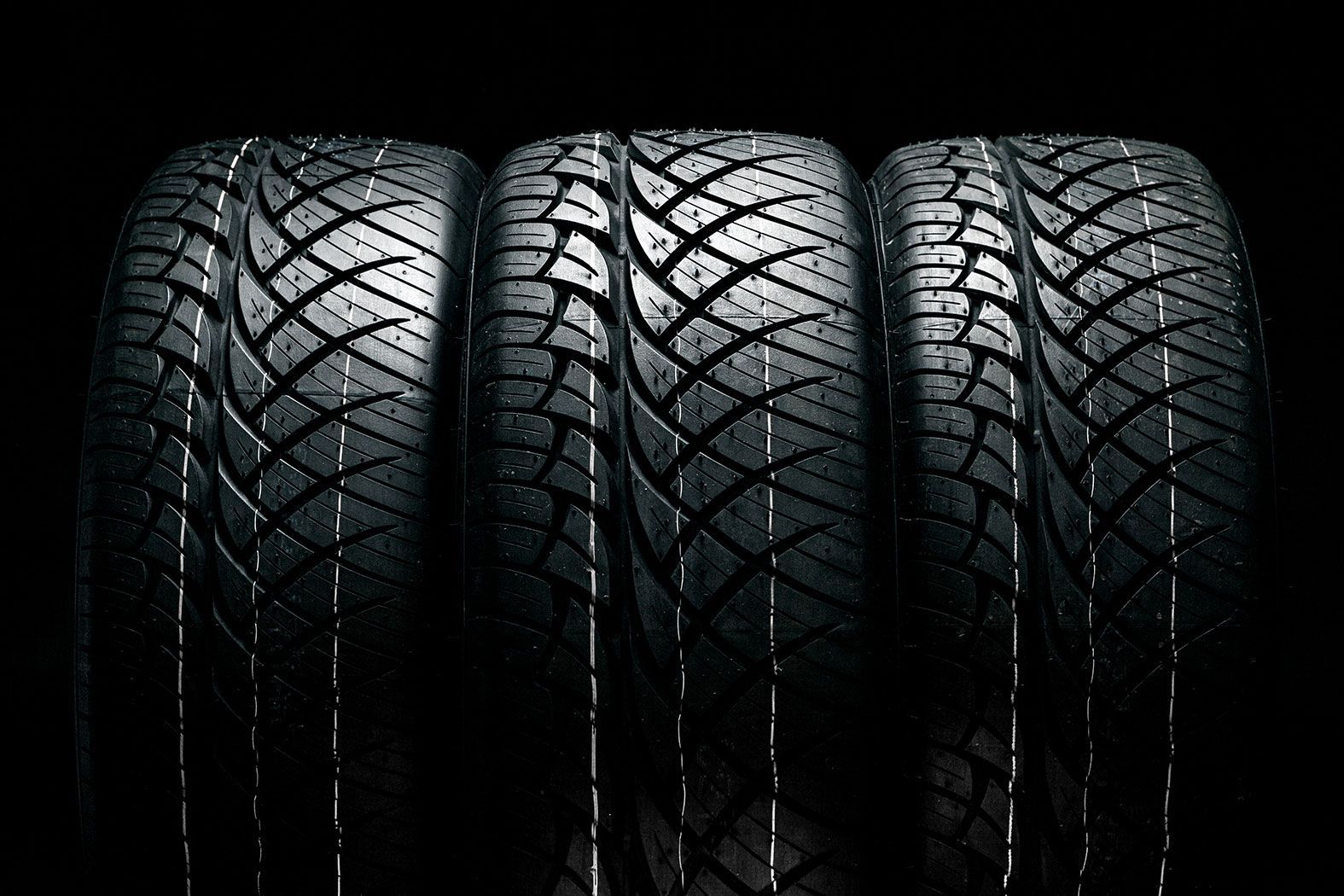 Mechanic smiles while working on car engine in shop, wearing safety glasses and gloves.