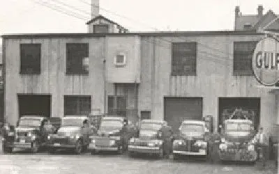 Black and white photo of a vintage garage with six parked cars in front. A Gulf sign hangs on the right.