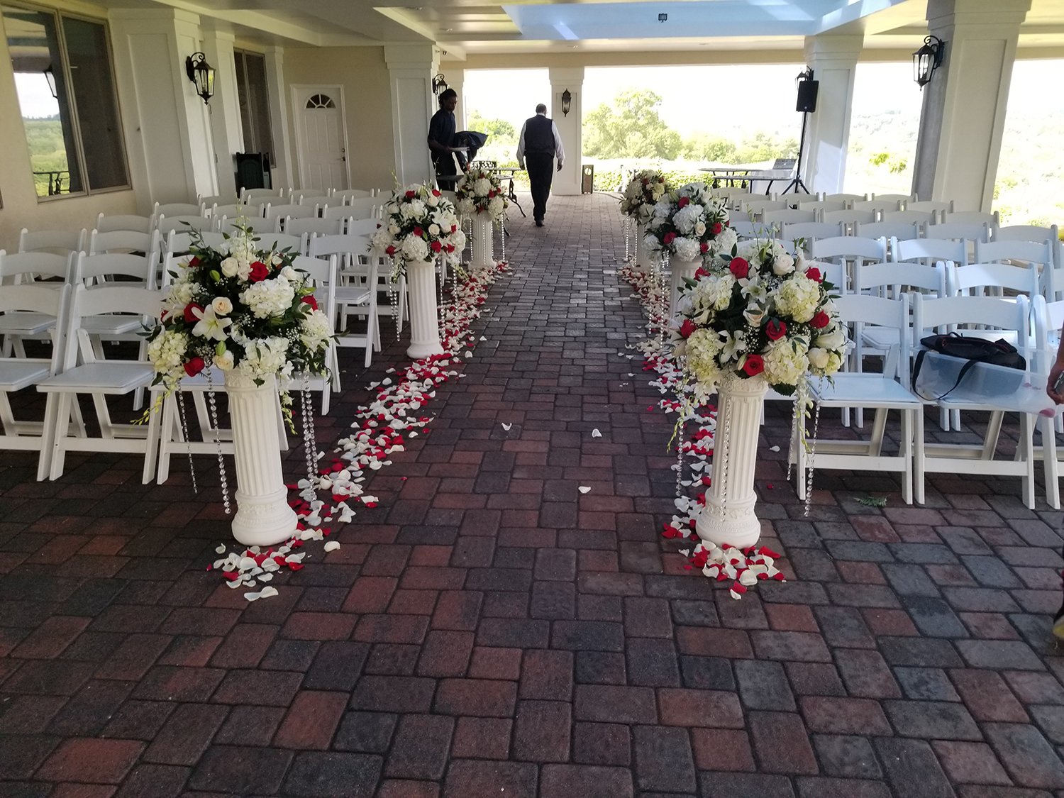 A brick walkway lined with white chairs and flowers