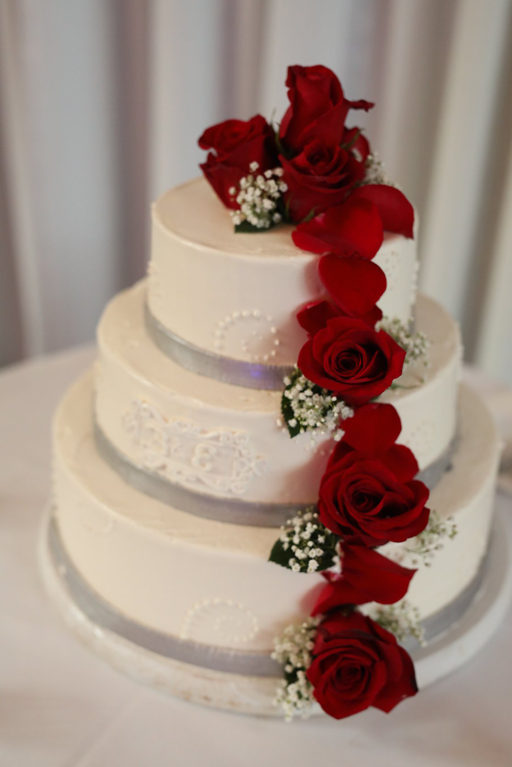 A white wedding cake decorated with red roses and baby 's breath