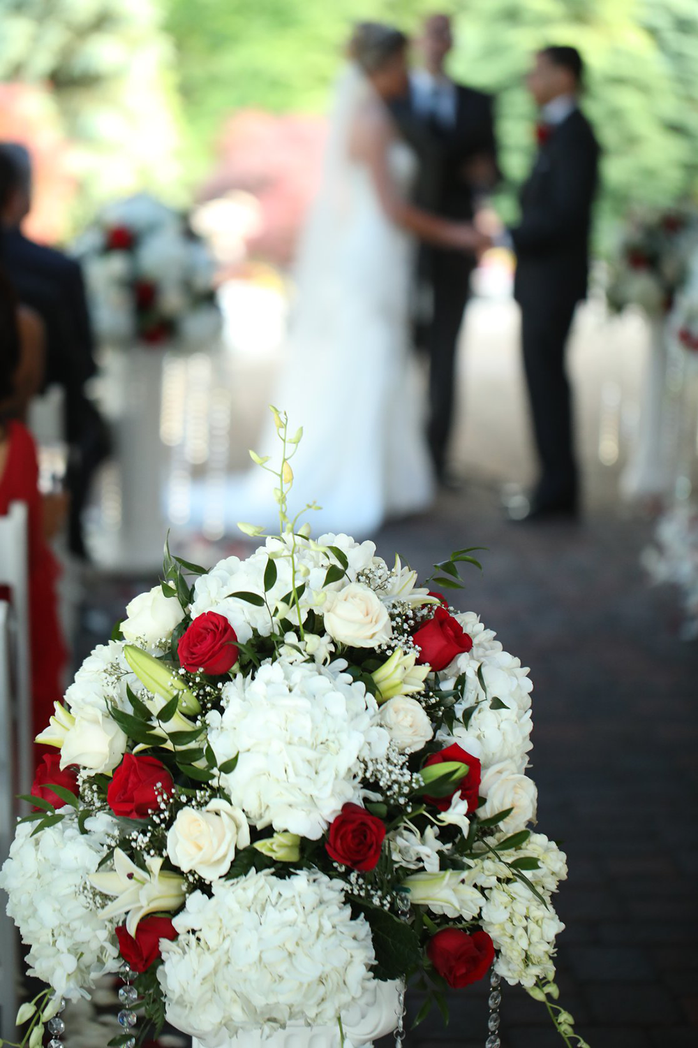 A bride and groom are standing in the background of a wedding ceremony with flowers in the foreground.