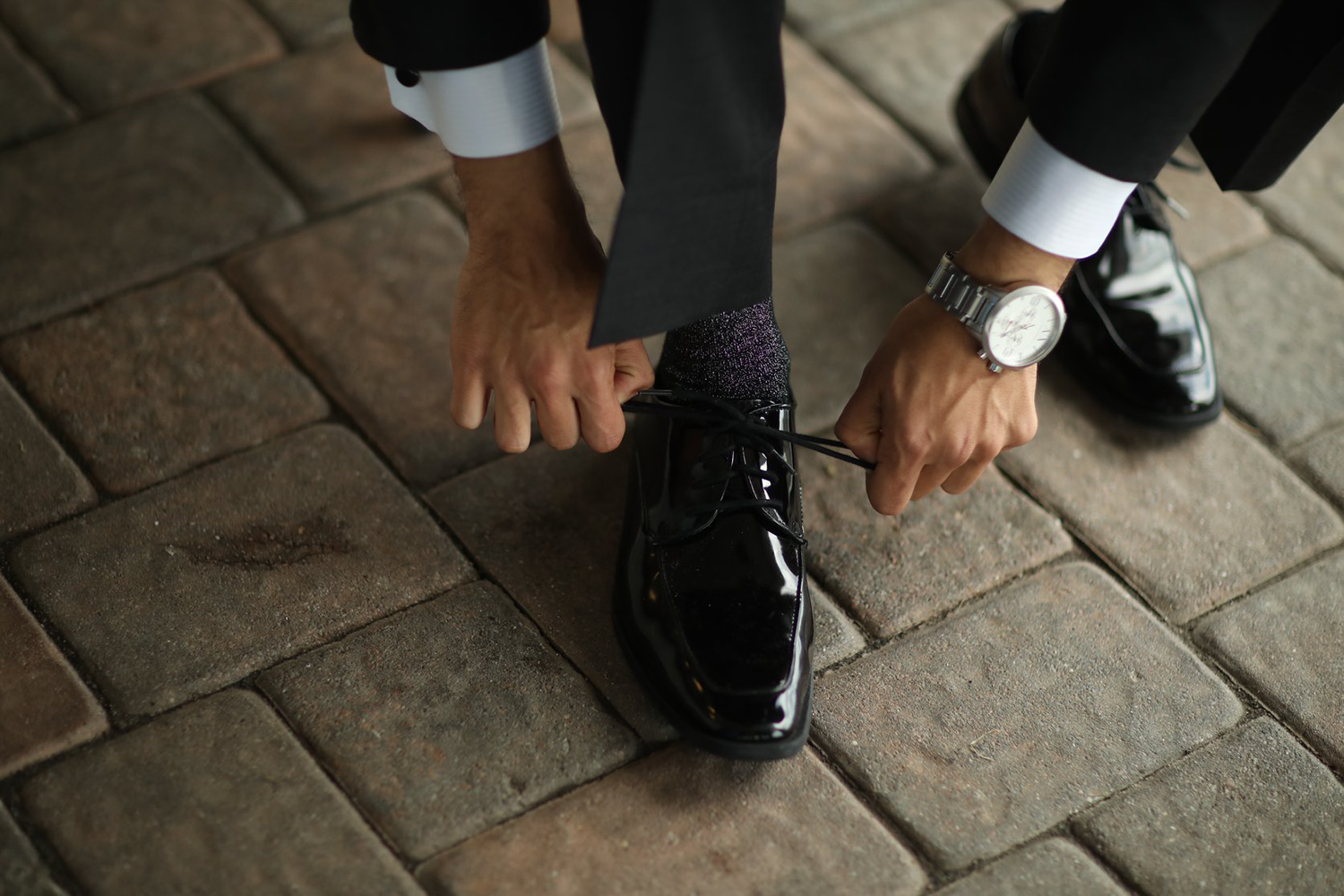 A man in a suit is tying his shoes on a brick sidewalk.