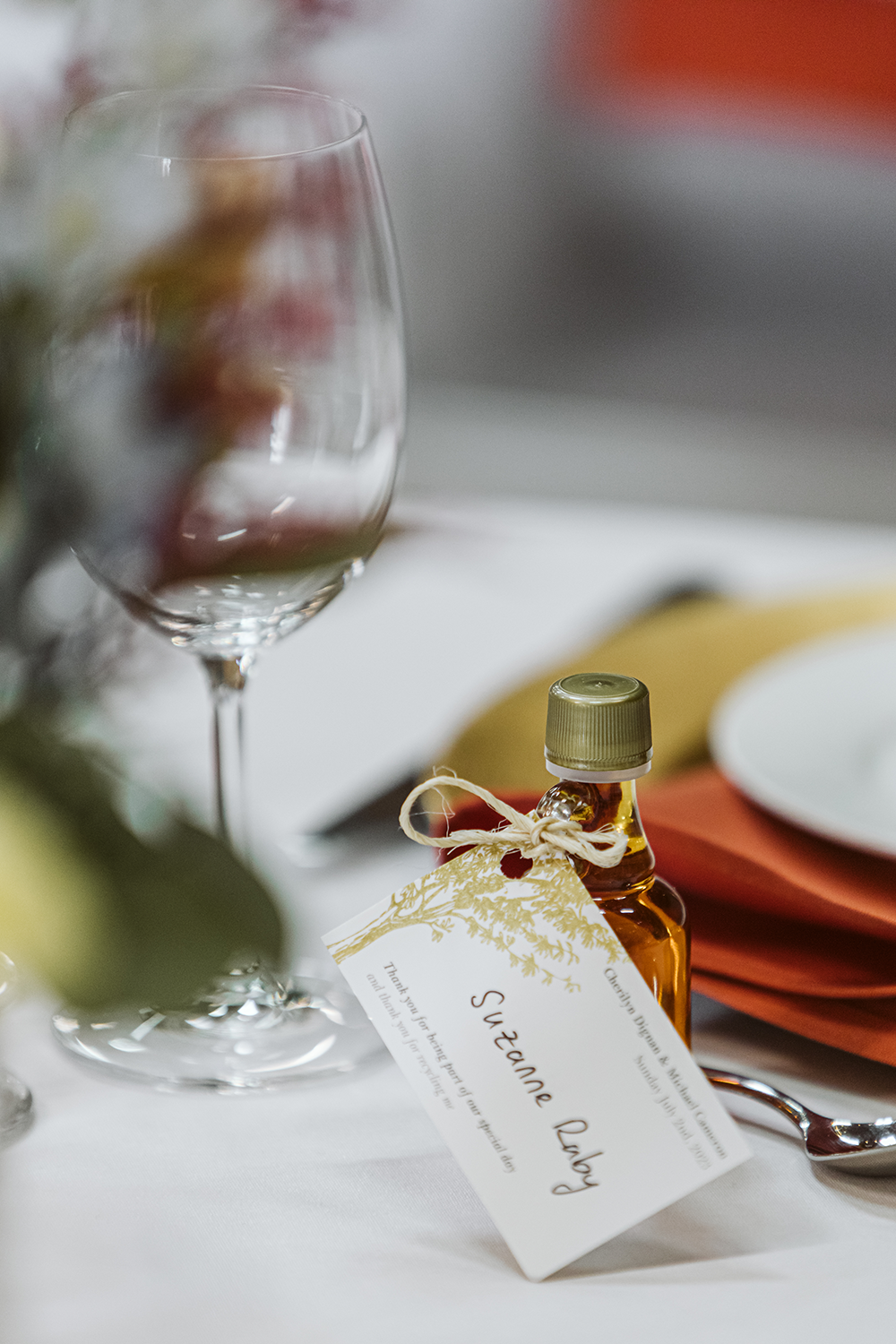 A small bottle of syrup is sitting on a table next to a wine glass.