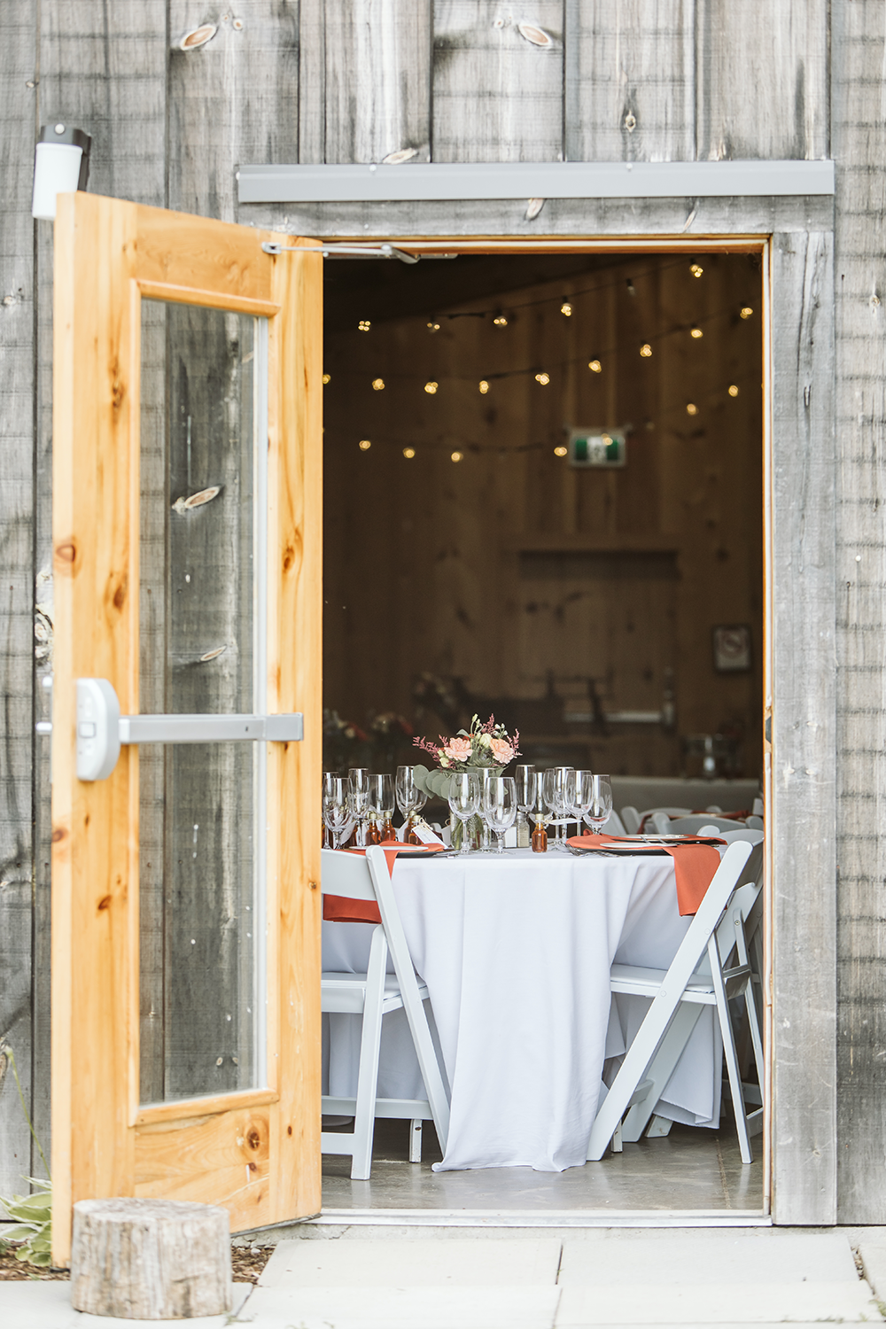 A wooden door is open to a room with tables and chairs set up for a wedding reception.