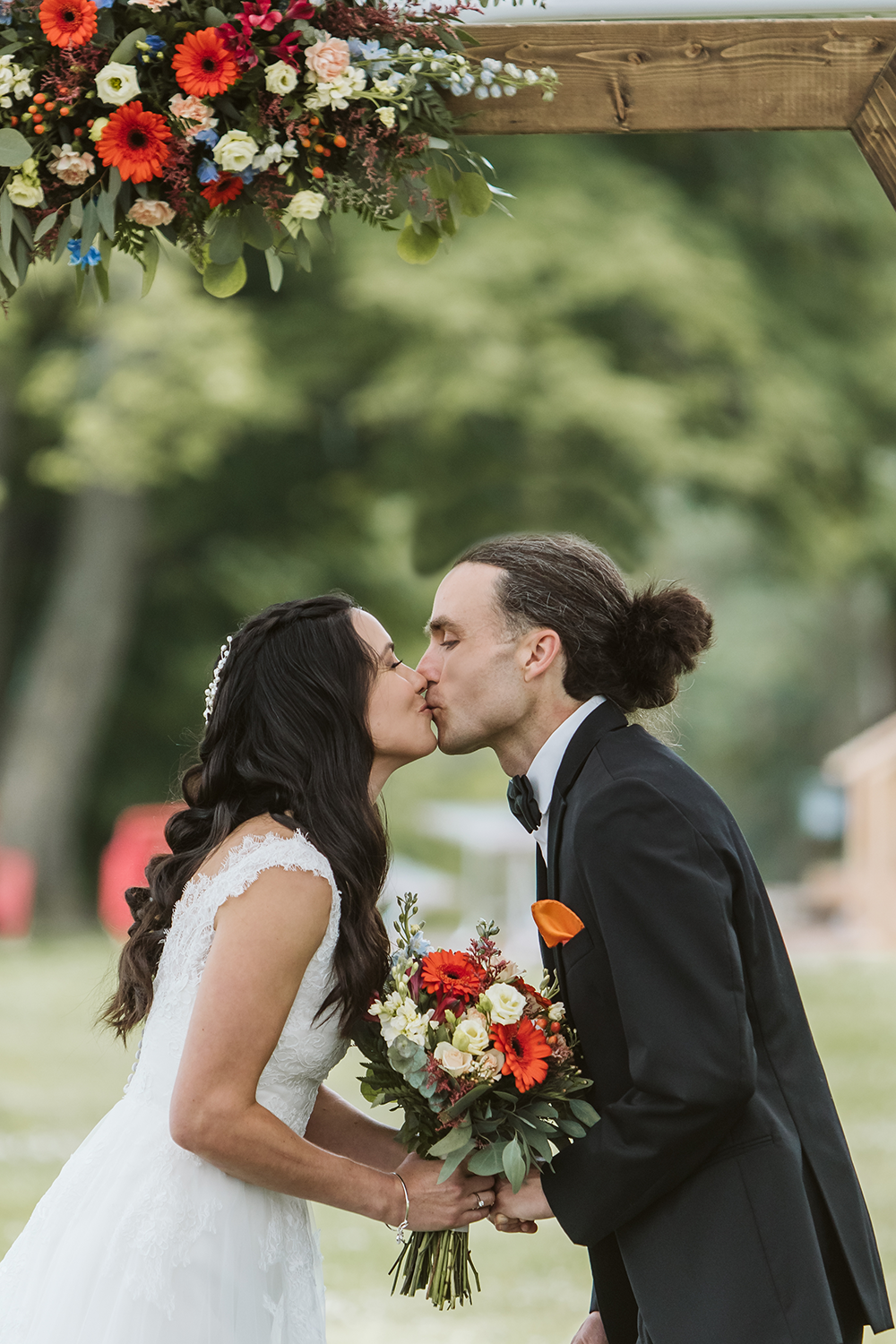 A bride and groom are kissing under a wooden arch at their wedding.