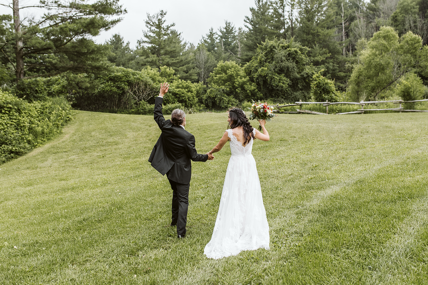 A bride and groom are walking through a grassy field holding hands.